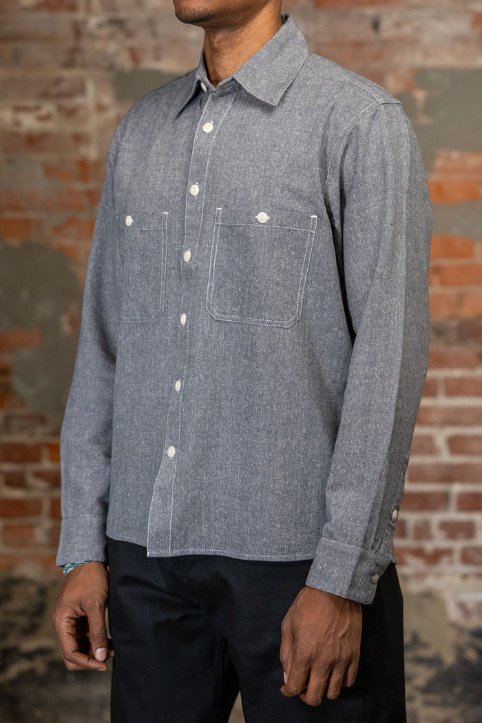 A person shown from the side wearing the 3sixteen Utility Chambray Shirt - Handloom Silk Khadi, while standing in front of a rustic brick wall.