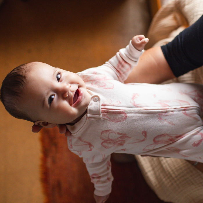 Baby wearing a white footed romper with pink ballet slipper print