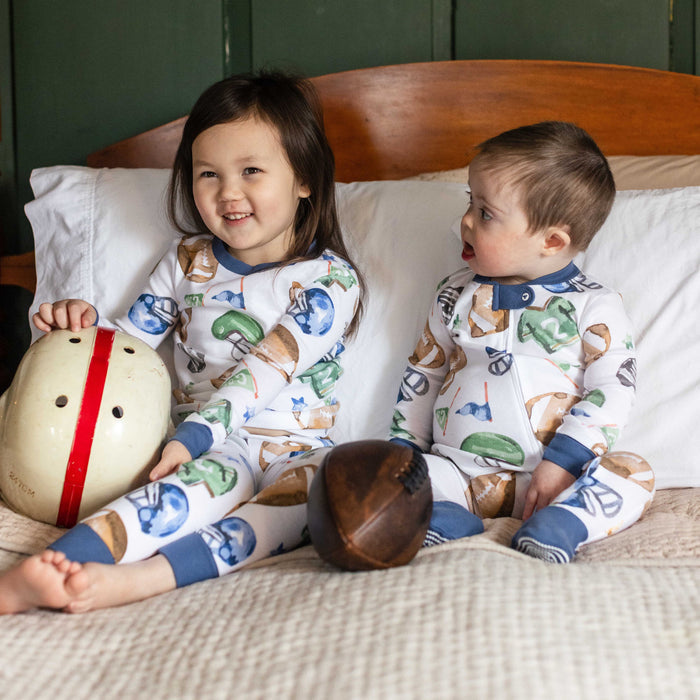 Football-print footed sleepers on two toddlers with navy cuffs and snap neck