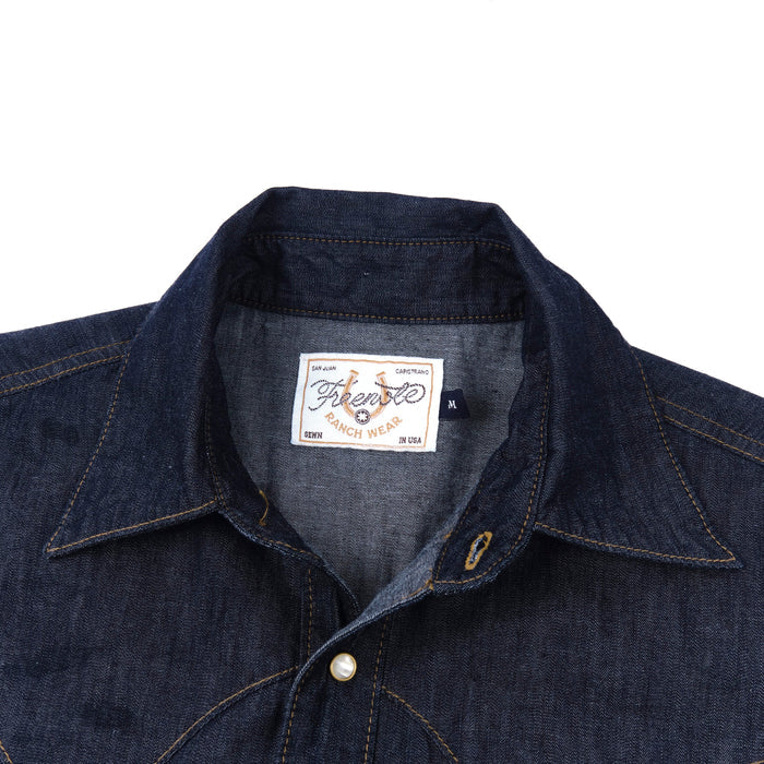 Dark indigo denim western-style short sleeve shirt with white snaps, close up on collar laying flat