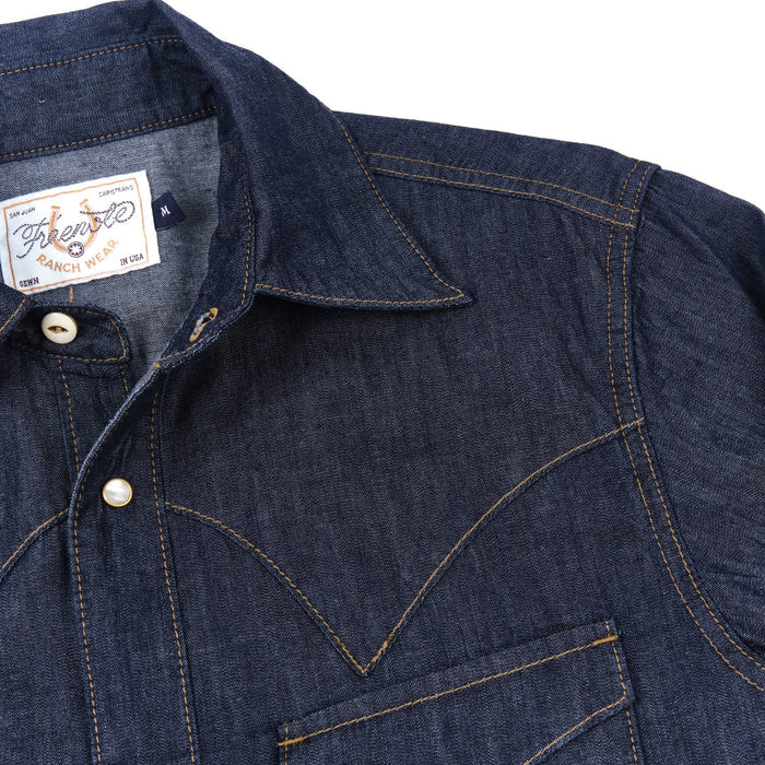 Dark indigo denim western-style short sleeve shirt with white snaps, close up on shoulder laying flat