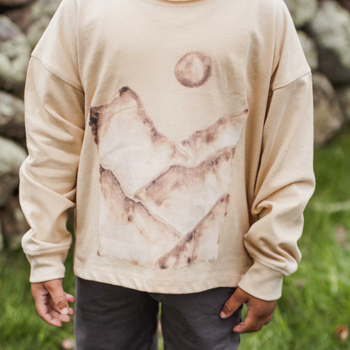 Kids long-sleeve tee close-up: cream with watercolor mountain graphic and circle moon