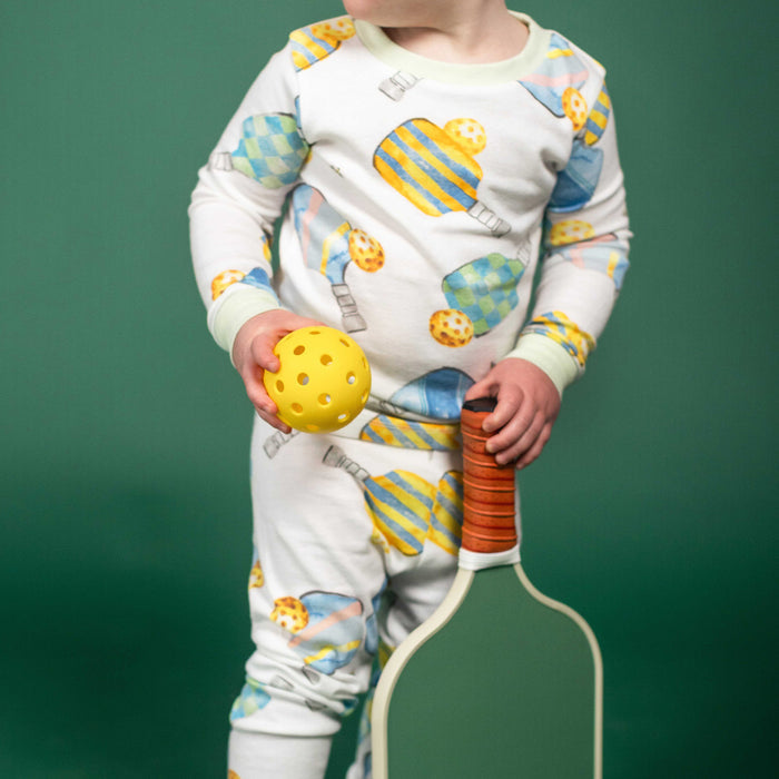 Child wearing white long-sleeve pajamas with blue and yellow pickleball print