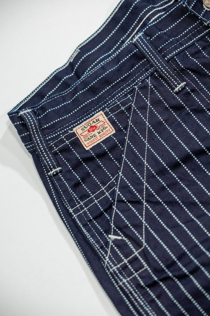 Navy striped fatigue pocket pants close up on right front pocket with white/red Sugar Cane logo laying flat