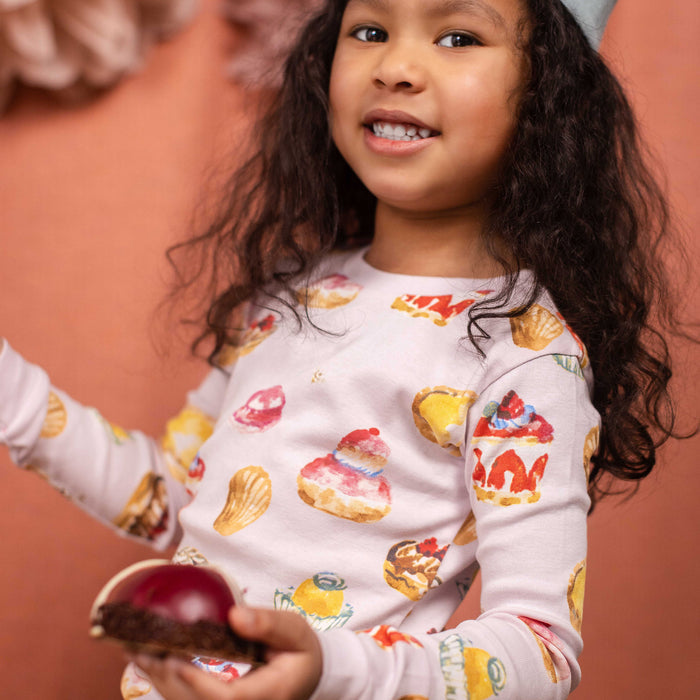 Child wearing long-sleeve pajama top and matching pants with colorful pastry graphics