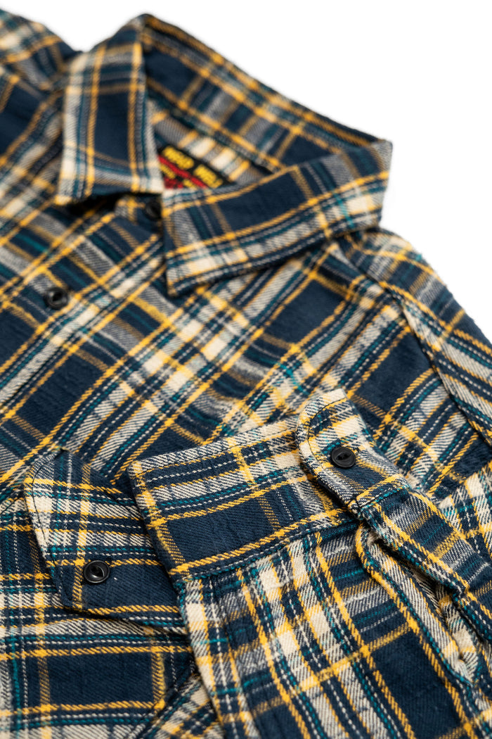 UES 502655 Slubby Flannel Shirt - Navy Close-up of a plaid button-up shirt in navy blue, yellow, and white, showing the collar, front buttons, and fabric texture against a white background.